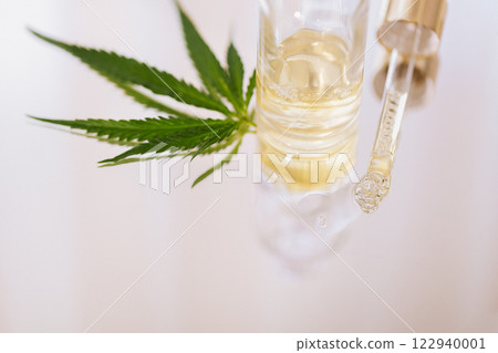 Mock up bottle cosmetic product and pipette with cannabis leaves on white glossy background. Yellow moisturizing facial serum with hyaluronic acid and hemp leaf on marble table. 122940001
