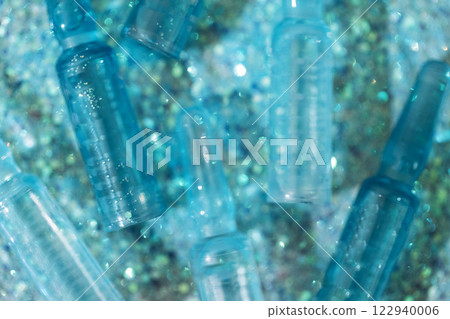Close-up of blue ampoules with intense moisturizing concentrate with hyaluronic acid and vitamins on shiny sparkling background. Close-up of blue ampoules with intense moisturizing concentrate with hyaluronic acid and vitamins on shiny sparkling background. 122940006