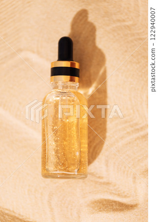 A mock-up glass bottle with a pipette with an intensive moisturizing concentrate with hyaluronic acid and vitamins on a background of sand. 122940007