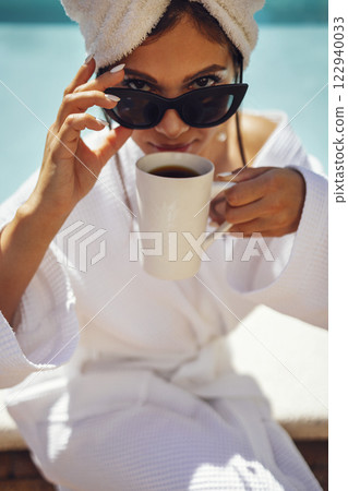 Young pretty woman in a white bathrobe holds a cup of coffee. Young pretty woman in a white bathrobe holds a cup of coffee. 122940033