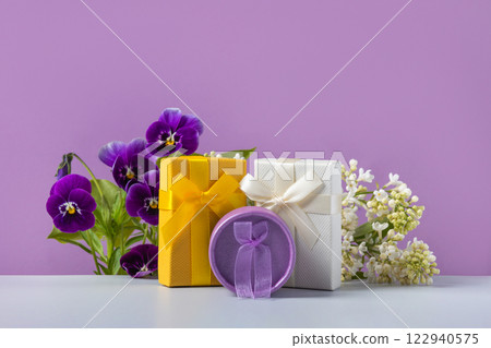 A spring greeting composition of purple viola flowers and cherry blossom branches with yellow, white and purple gift boxes on gray table. Concept of spring, Easter, Mother's Day, happy Valentine's Day 122940575