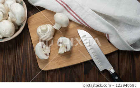 Fresh champignon mushrooms. Cutting champignon on cutting board. 122940595