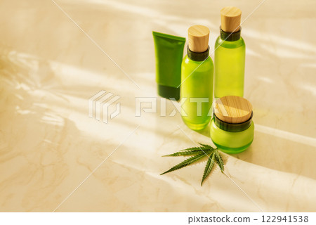 Green cosmetic bottles with wooden caps and hemp leaf on marble surface. Green cosmetic bottles with wooden caps and hemp leaf on marble surface. 122941538