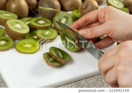 The process of cutting fresh ripe kiwi into slices with a knife. 122942149