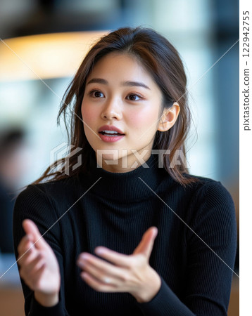 Asian woman in black turtleneck gestures while speaking, expressing engagement and focus Asian woman in black turtleneck gestures while speaking, expressing engagement and focus 122942755