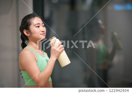 A young woman hydrates between workouts at an indoor gym A young woman hydrates between workouts at an indoor gym 122942934
