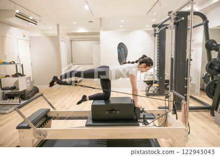 Young woman doing machine pilates in indoor gym Young woman doing machine pilates in indoor gym 122943043