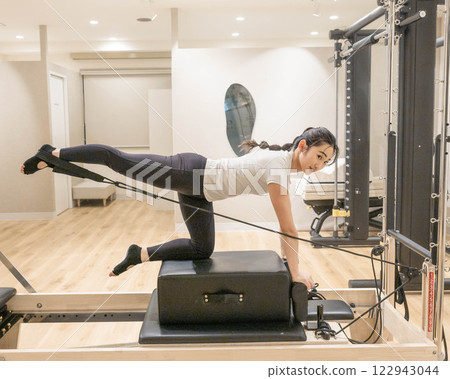 Young woman doing machine pilates in indoor gym 122943044