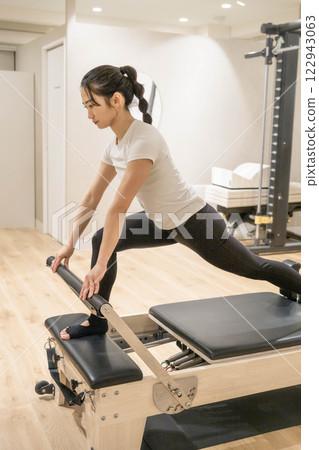 Young woman doing machine pilates in indoor gym Young woman doing machine pilates in indoor gym 122943063
