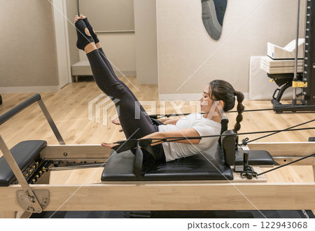 Young woman doing machine pilates in indoor gym Young woman doing machine pilates in indoor gym 122943068