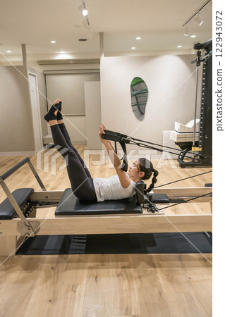 Young woman doing machine pilates in indoor gym Young woman doing machine pilates in indoor gym 122943072