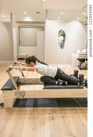 Young woman doing machine pilates in indoor gym Young woman doing machine pilates in indoor gym 122943082