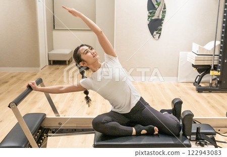 Young woman doing machine pilates in indoor gym Young woman doing machine pilates in indoor gym 122943083