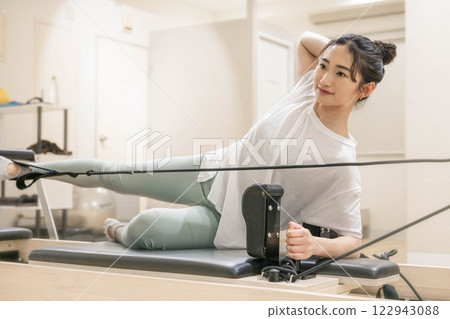 Young woman doing machine pilates in indoor gym 122943088