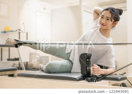 Young woman doing machine pilates in indoor gym Young woman doing machine pilates in indoor gym 122943091
