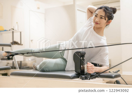 Young woman doing machine pilates in indoor gym Young woman doing machine pilates in indoor gym 122943092