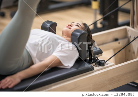 Young woman doing machine pilates in indoor gym 122943095