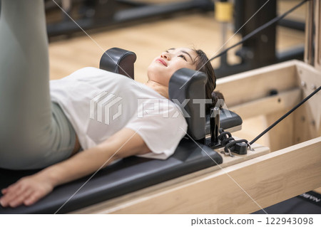 Young woman doing machine pilates in indoor gym Young woman doing machine pilates in indoor gym 122943098