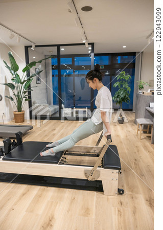 Young woman doing machine pilates in indoor gym Young woman doing machine pilates in indoor gym 122943099
