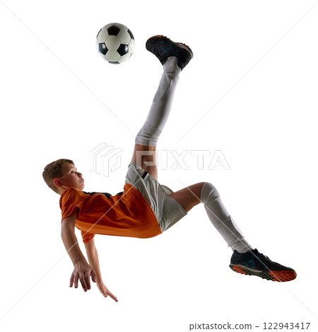 Boy in orange jersey and white shorts, flipping mid-air, executing acrobatic bicycle kick, training against white studio background. 122943417