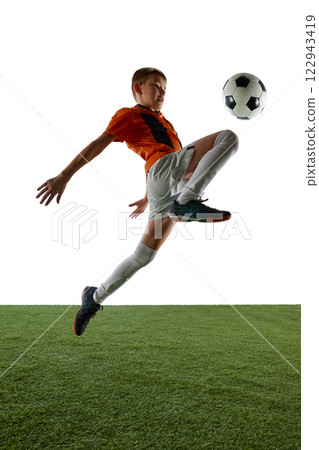 Dynamic image of boy in orange jersey and white shorts in motion, kicking ball with knee, training against white background 122943419