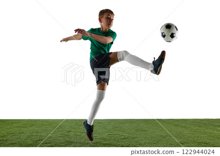Dynamic image of boy, soccer player in green jersey and black shorts in motion during training session, playing, kicking ball against white background. 122944024