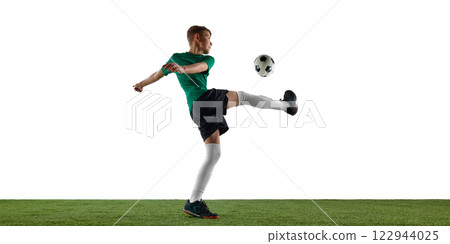 Dynamic image of boy, soccer player in green jersey and black shorts in motion during training session, playing, kicking ball against white background. 122944025