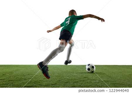Boy in green jersey, black shorts, white socks, viewed from behind, running towards soccer ball against white studio background. Boy in green jersey, black shorts, white socks, viewed from behind, running towards soccer ball against white studio background. 122944040