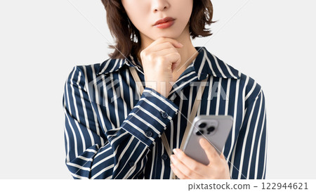 Woman/businesswoman thinking while looking at her smartphone Woman/businesswoman thinking while looking at her smartphone 122944621