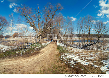 Early spring in the countryside. Spring rural landscape with a stream. Dirt road on the dam 122945415