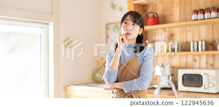 A woman in an apron thinking in the kitchen A woman in an apron thinking in the kitchen 122945636