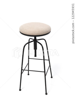 A simple beige upholstered stool with a black metal frame, featuring adjustable height. 122945931