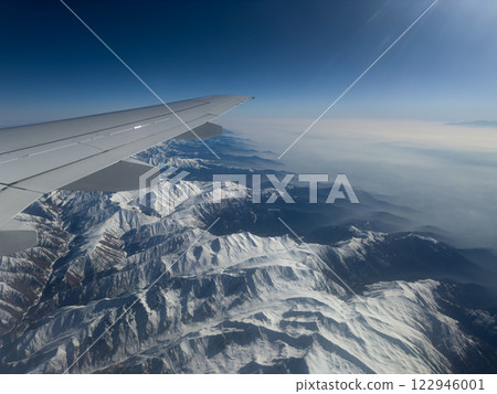 Impeccable view from airplane window while flying over massive mountain ranges in snow. Stunning view from airplane window. The best seats on plane are at wing with beautiful view of mountains Impeccable view from airplane window while flying over massive mountain ranges in snow. Stunning view from airplane window. The best seats on plane are at wing with beautiful view of mountains 122946001