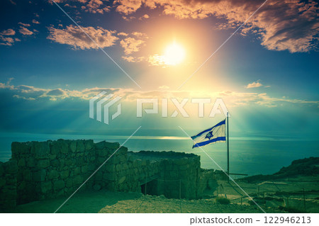 Beautiful sunrise over Masada fortress. Ruins of King Herod's palace in the Judaean Desert. The flag of Israel fluttering on Masada 122946213