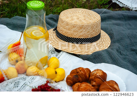 Picnic on a summer day with straw hat, refreshing lemonade, fresh fruit, and croissants on blanket 122946623