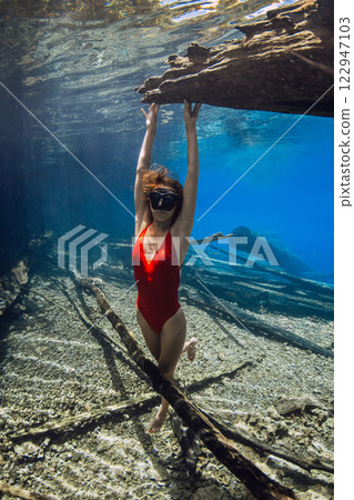 Woman freediver posing underwater with woden logs in the lake. Free diving in crystal clear lake Woman freediver posing underwater with woden logs in the lake. Free diving in crystal clear lake 122947103