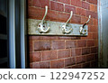 Old coat hooks on wooden board against brick wall 122947252