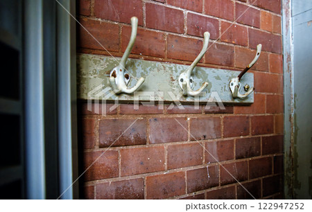 Old coat hooks on wooden board against brick wall 122947252