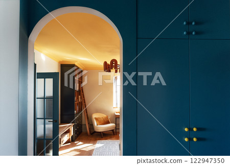 Cozy stylish interior of the living room. An arched doorway with a bright blue wall and a built-in wardrobe. Contrasting design with natural wooden furniture. 122947350