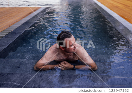 A young attractive man is swimming in an indoor pool. A handsome guy is relaxing on the side of the pool. Water sports activities. A young attractive man is swimming in an indoor pool. A handsome guy is relaxing on the side of the pool. Water sports activities. 122947362