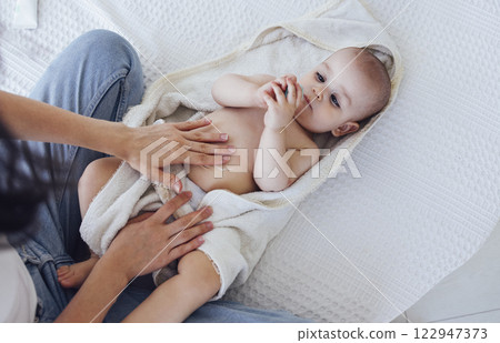 Sweet cute baby sits on the bed next to his mom and plays after bath 122947373