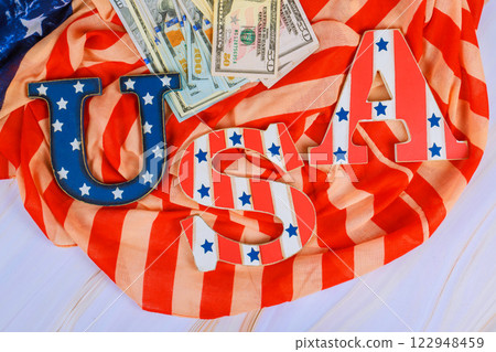 USA letters sit top striped fabric with dollar bills, symbolizing patriotism finance celebration. 122948459