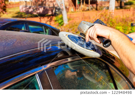 Technician worker is using buffing tool to polish top of dusty car in car service garage Technician worker is using buffing tool to polish top of dusty car in car service garage 122948498