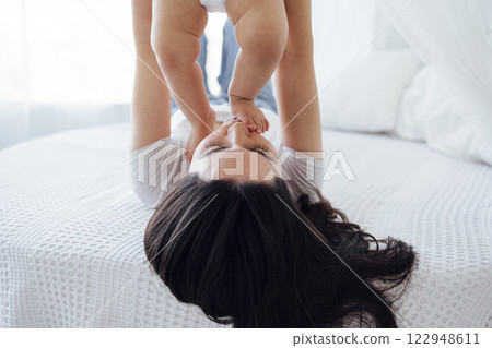 Pretty infant in a white bodysuit with his mom on a light background. 122948611