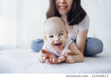 Pretty infant in a white bodysuit with his mom on a light background. Motherhood concept. Pretty infant in a white bodysuit with his mom on a light background. Motherhood concept. 122948613