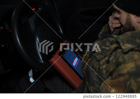Professional car mechanic using specialized computer software to diagnose and troubleshoot electronic systems within a vehicle, highlighting modern automotive repair techniques. 122948895