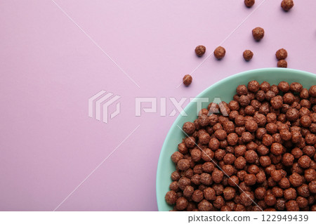 Chocolate cereal corn balls in a blue bowl on a purple background. Chocolate cereal corn balls in a blue bowl on a purple background. 122949439
