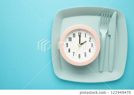 Top view of pink alarm clock with plate, fork and knife on blue background - concept and idea 122949470