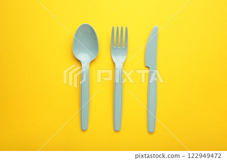 Blue plasic forks, spoons and knives on yellow background with copy space, top view. Blue plasic forks, spoons and knives on yellow background with copy space, top view. 122949472