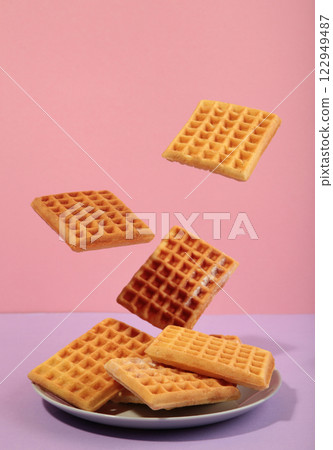 Belgian waffles flying in air on a pasel pink background. Waffles in plate. Creative food concept. Belgian waffles flying in air on a pasel pink background. Waffles in plate. Creative food concept. 122949487